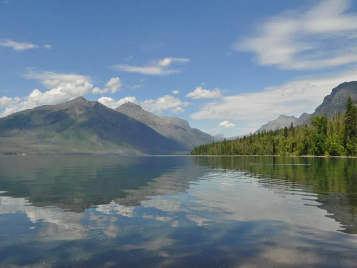 reflective lake McDonald glacier national park Montana with trees and mountains in distance