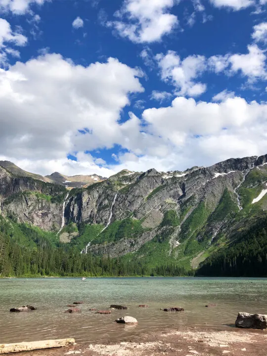 green lake with jagged mountains in the distance with white puffy clouds at Avalanche Lake Montana