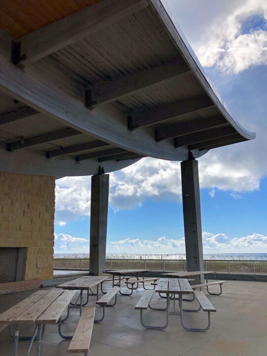 Gulf State Park pavilion with picnic tables under large awning and ocean in distance
