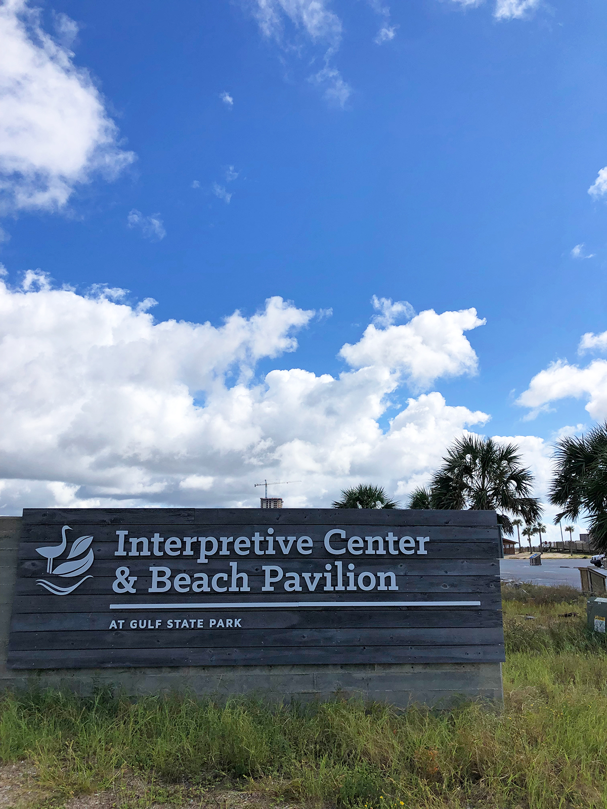 sign that reads interpretive center and beach pavilion at gulf state park with white puffy clouds