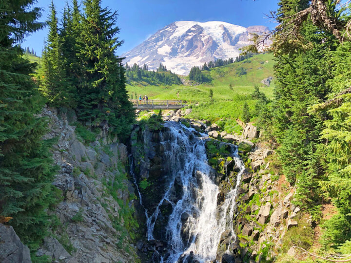 things to do in mt rainier visit a waterfall with trees alongside bridge above and mountain in distance