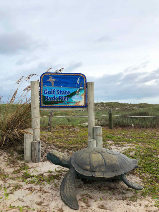 sign for Gulf State Park pier with large fake turtle on cloudy day