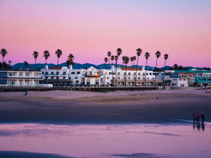 San Francisco to San Diego road trip stop at beautiful pink beach at dusk with buildings palm trees and people