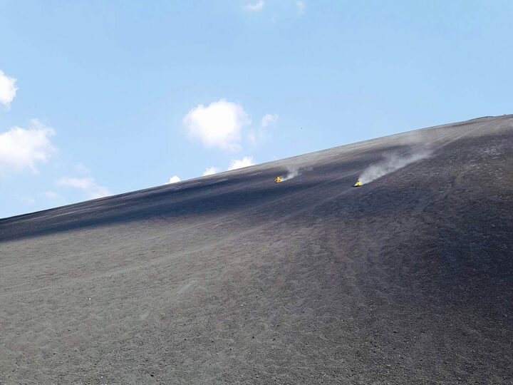 adventure bucket list view of volcano boarding in Nicaragua two people in the distance sliding down huge black volcano