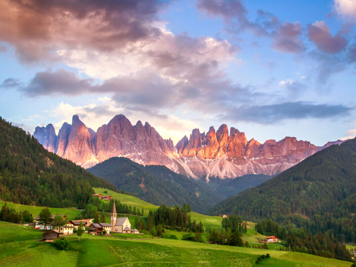 view of dolomites adventurous getaways mountains with pink sunset and green valley with church