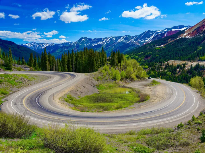 view of curvy road with mountains in background blue sky lots of greenery