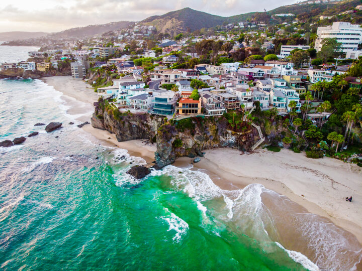 Laguna Beach shore from above with green water, sandy beach and large homes on a cliff