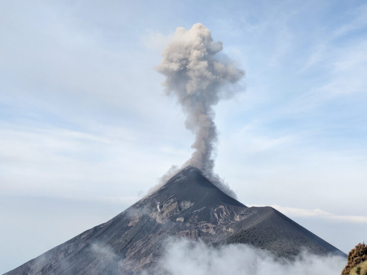 gray pyramid shaped volcano with puff of steamy smoke rising into the air
