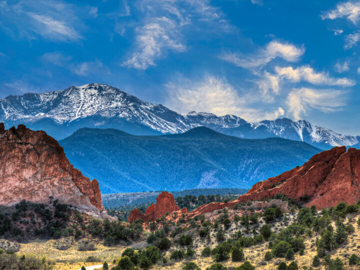 red rocks and trees with mountains in background with blue sky