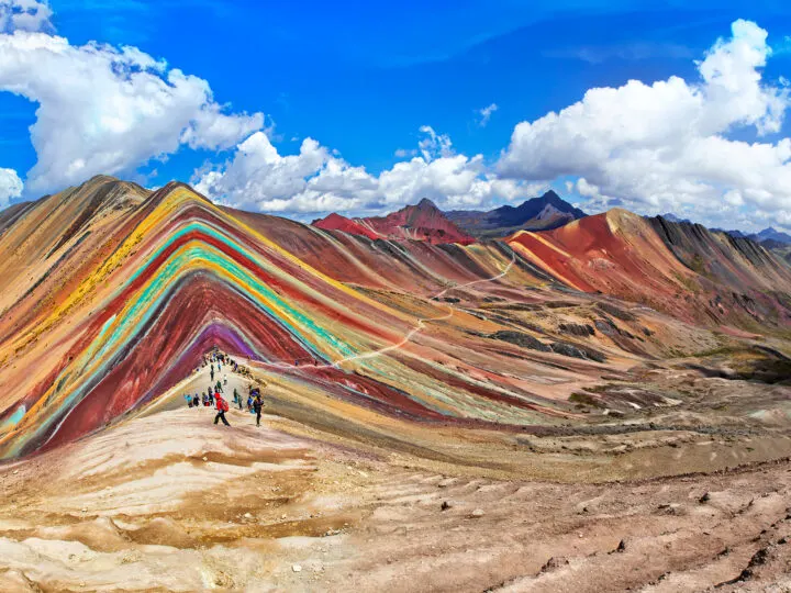 view of brightly colored mountain with rainbow stripes blue sky and people in distance