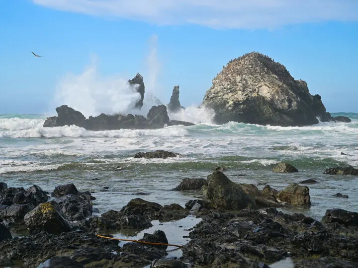 pacific coast highway itinerary stops along rocky coast with water and waves splashing on large boulder