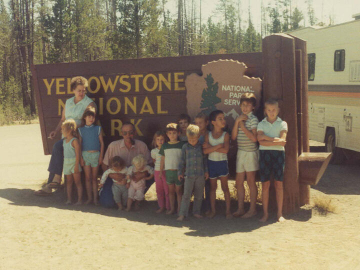 family standing in front of the Yellowstone National park sign with RV in background