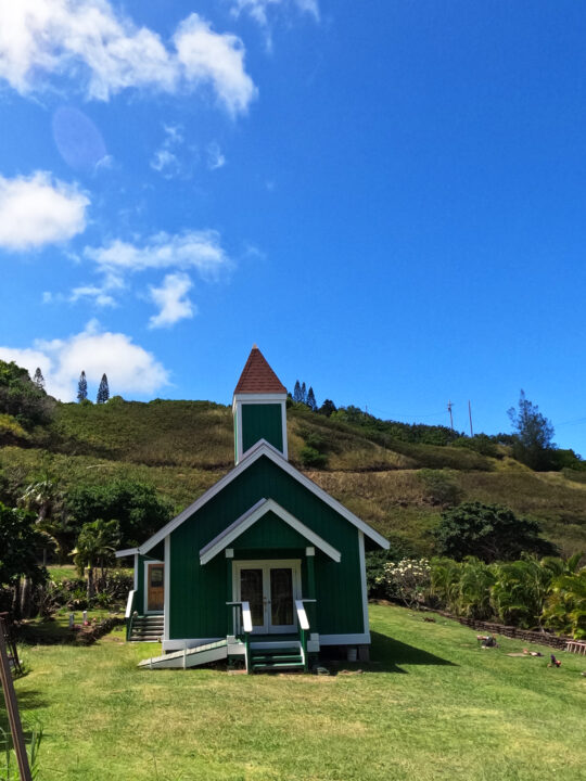 green church with white trim on hillside with blue sky