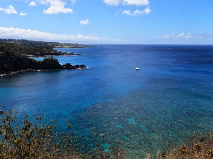 view of Honolua Bay Maui bright blue water with coral reef coastline and boat