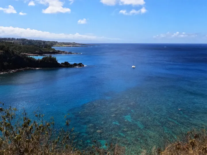 view of Honolua Bay Maui bright blue water with coral reef coastline and boat best places to visit in November