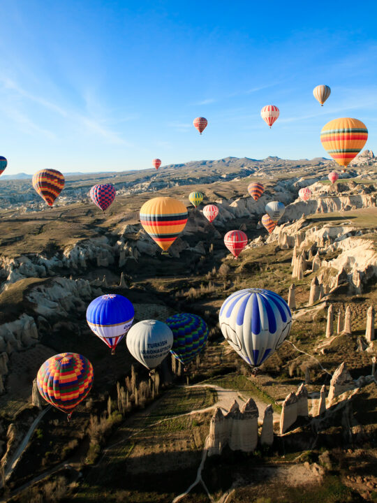 lots of hot air balloons over rocky terrain with blue sky