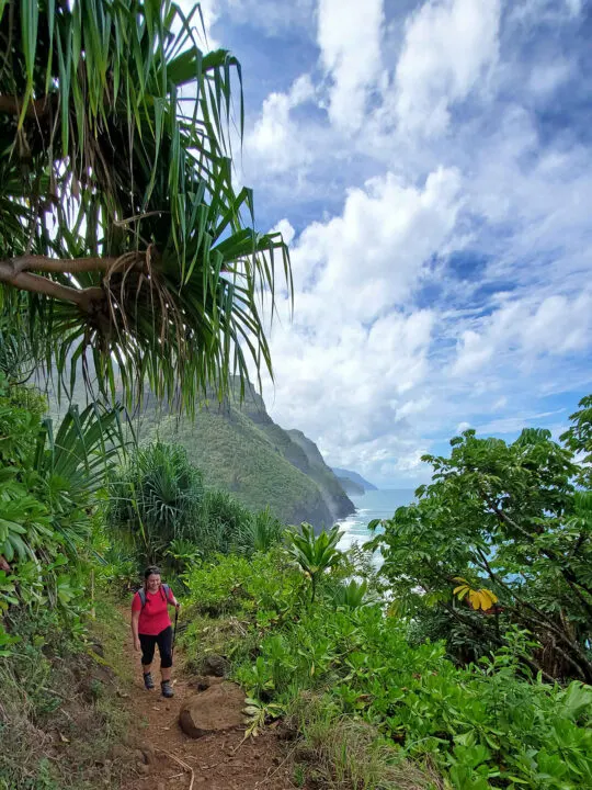 woman hiking the coastline in Hawaii cliffs and ocean with clouds