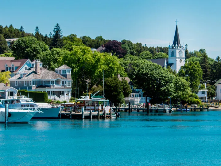 view of Mackinac Island in September with boats and houses along bay with trees and church steeple