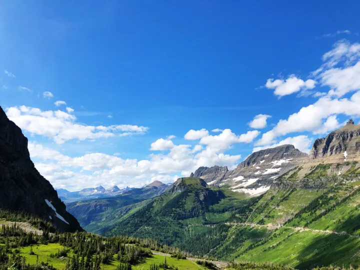 view in Glacier National Park with mountain peaks and lush greenery on sunny day