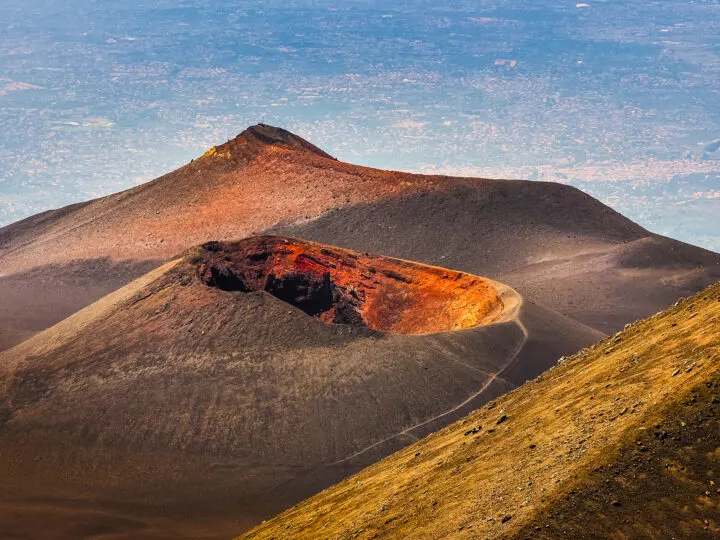volcano with black sand and crater in center with city in distance