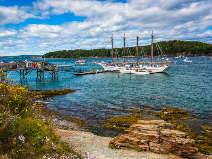 September vacations USA view of coastal Maine with ship in harbor rocky shore trees in distance