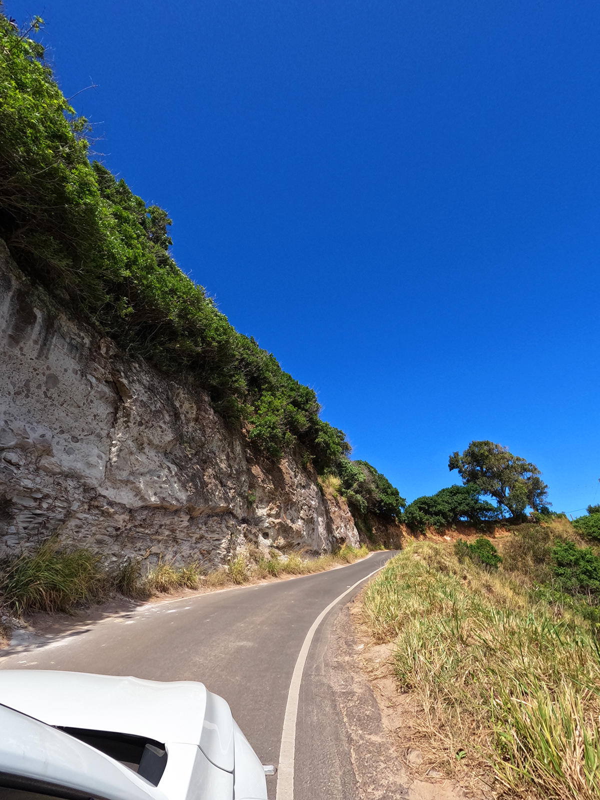 car on narrow road beside rocky cliff