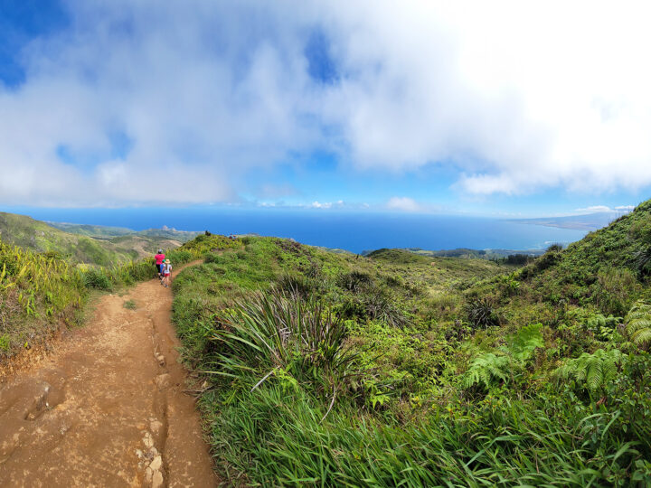 Ohai trail Kahekili Highway view of woman and child on dirt hiking path with scenic view of valley and ocean