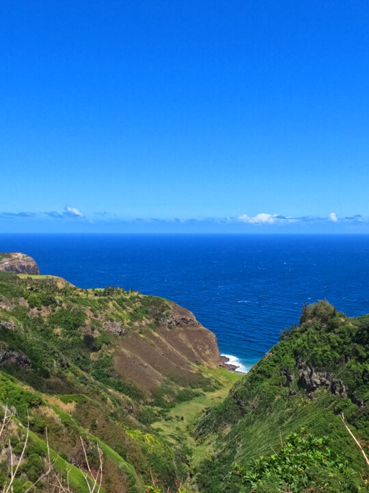 lush Maui ridges and valley leading out to ocean with blue water on sunny day