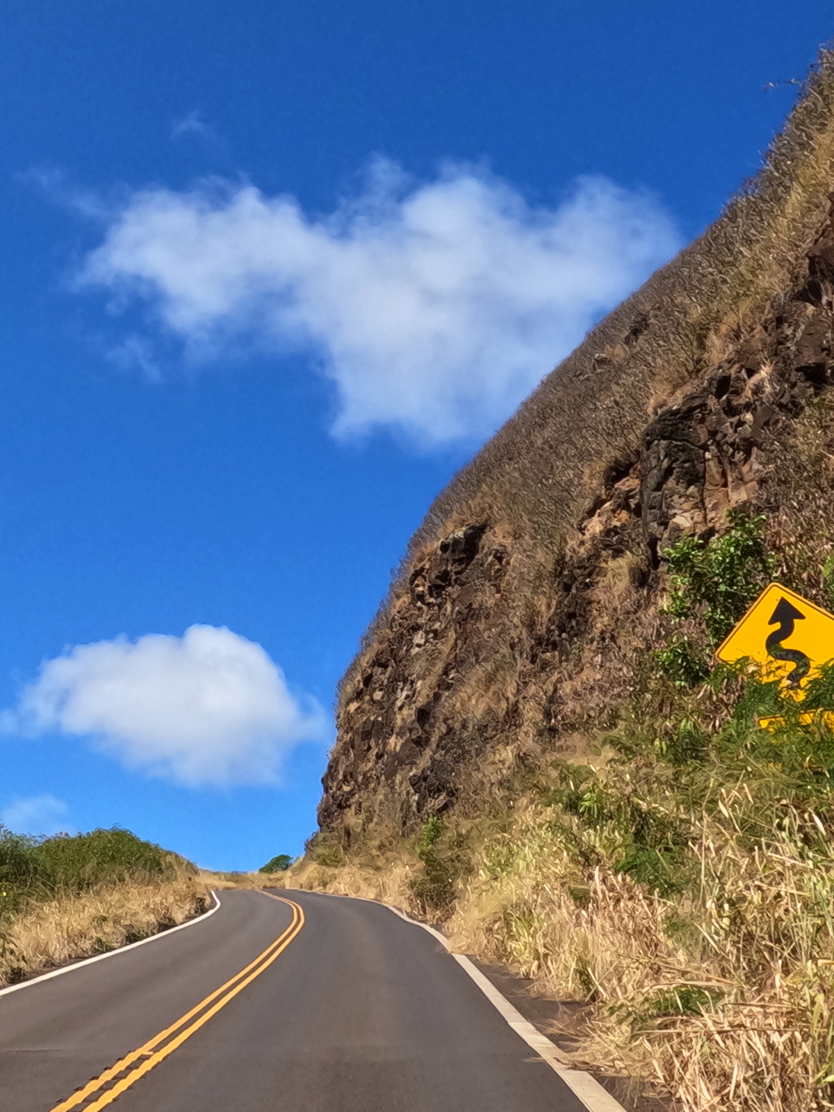 kahekili highway going uphill with yellow curvy road sign and cliff