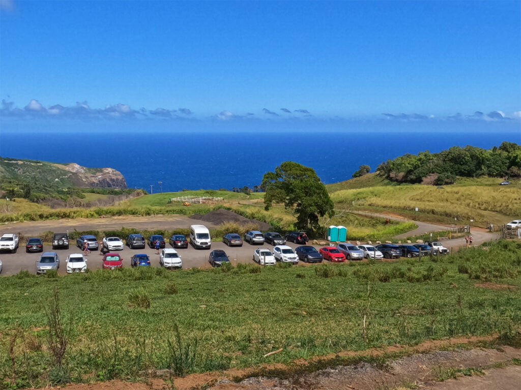 parking lot in distance with multi colored cars green space with ocean in distance