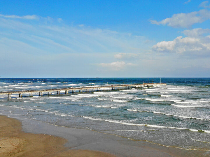 layers of ocean waves hitting the beach with small pier from above