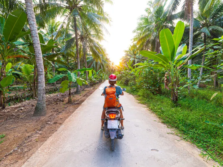 person with orange backpack riding scooter in palm tree lined area of Vietnam