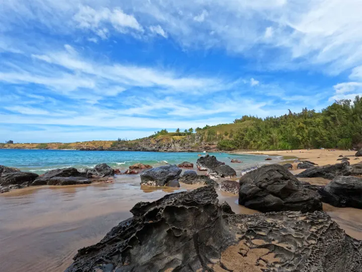 rocky beach with bright blue water tan sand and green hillside