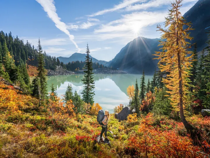 best national parks to visit in October lake and mountain scene with fall foliage and woman standing in front