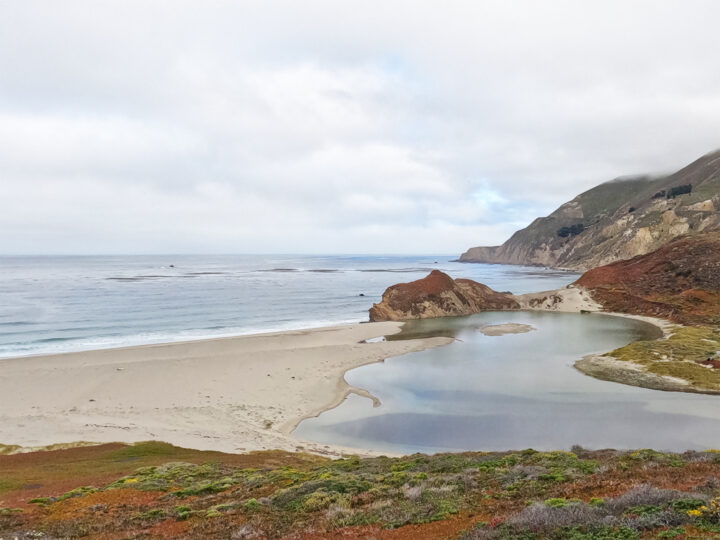 Big Sur drive view of coast with red bushes pond beside ocean and white clouds