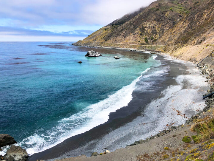 Big Sur california black sand beach teal water with road above