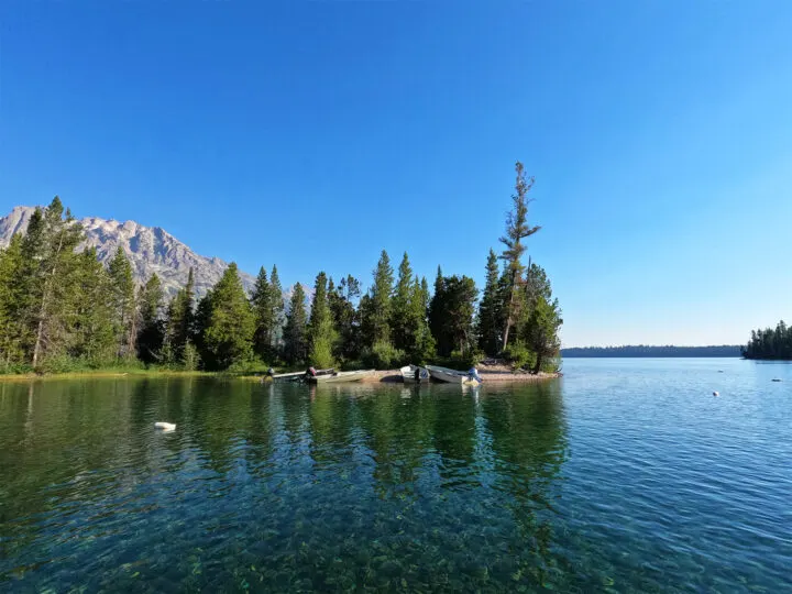 mountain lake scene with blue water boats at shore trees