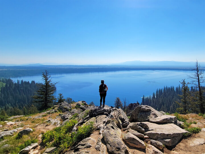 must see in grand teton national park view of a woman standing on cliff overlooking lake