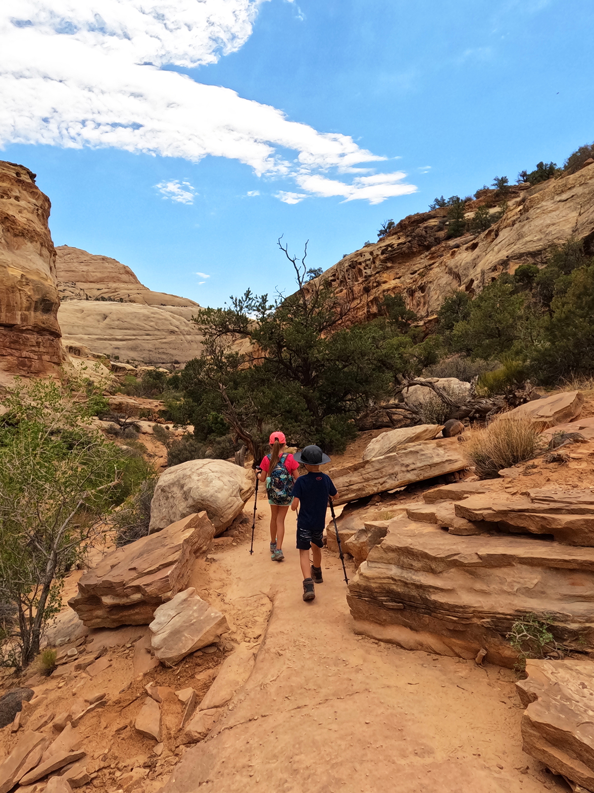 view of two kids hiking hickman bridge trail through rocky terrain