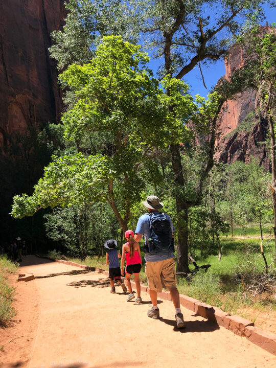 dad and two children hiking on dirt path with trees and red rocks