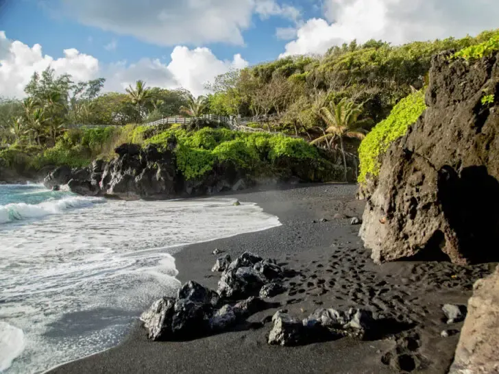 black sand beach epic maui road trip with green covered cliffs and ocean