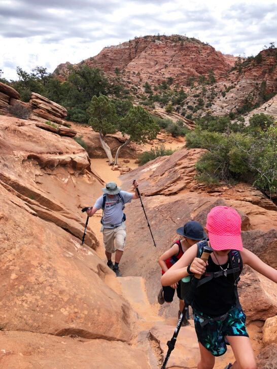 Zion canyon overlook man and two kids hiking through tight trail with slick rock nearby