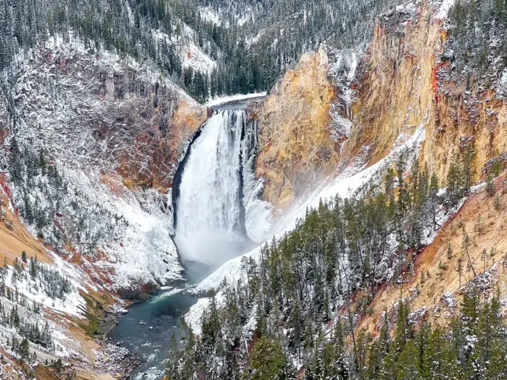 Yellowstone national park waterfall with snowy mountain cliffs nearby