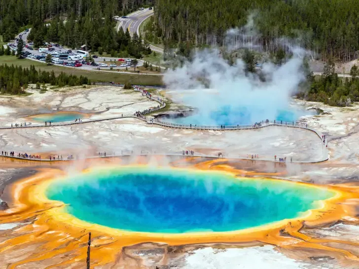multicolored prismatic spring with steam coming off it and parking lot in distance