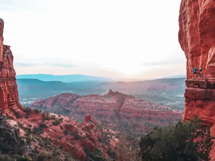 best American road trips view of large red rocks at sunset with hikers on ledge