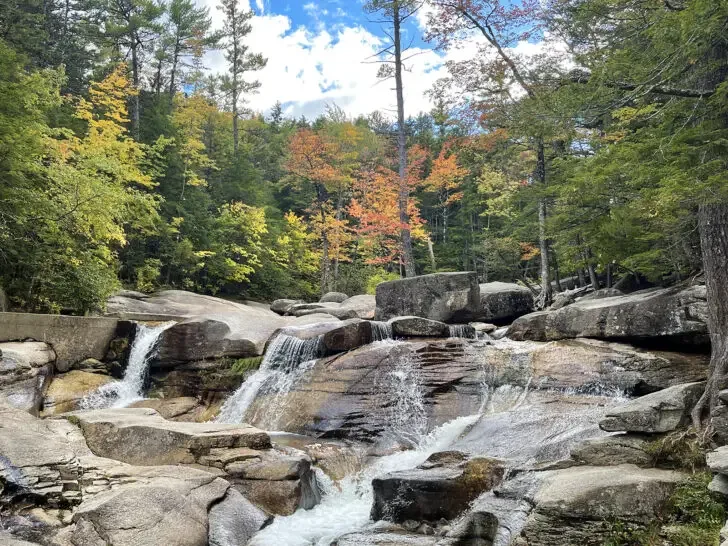 road trips USA stop along waterfalls over rocks with fall foliage in distance