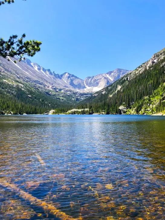 best national parks to visit in may lake with clear water and mountains in distance with trees and snow