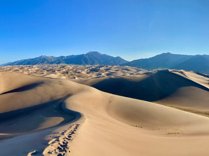 sand dunes with footprints and mountains in distance blue sky
