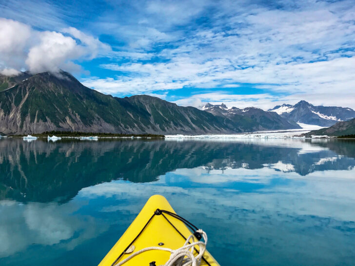 yellow kayak on blue water with mountains and glaciers in distance on the best USA road trip