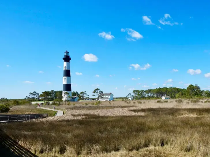 view of grassland with trees and lighthouse on sunny day best road trips USA